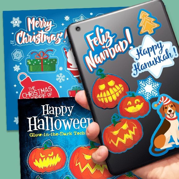 Hand holding tablet covered with tech tattoo labels with two sheets of holiday labels in background